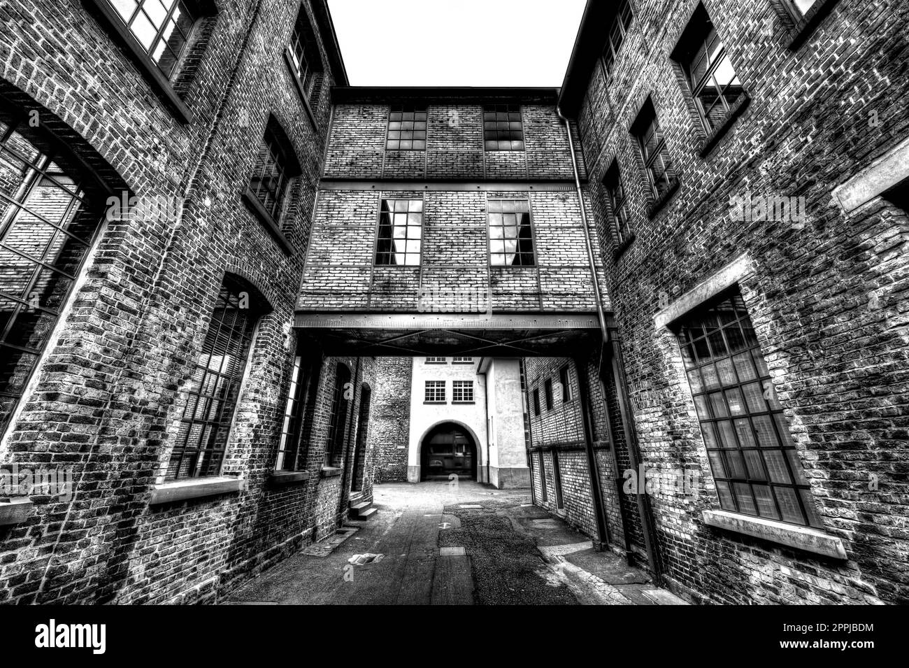 Der Durchgang zwischen zwei Ziegelhäusern im Hinterhof einer Fabrik in Schwarz-Weiß Stockfoto