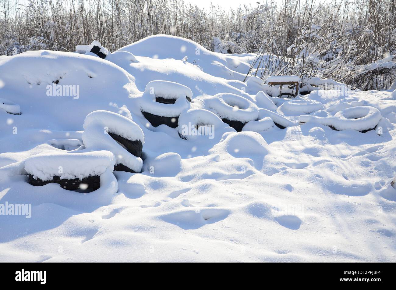 Gebrauchte und entsorgte Autoreifen liegen am Straßenrand und sind mit einer dicken Schneeschicht bedeckt Stockfoto