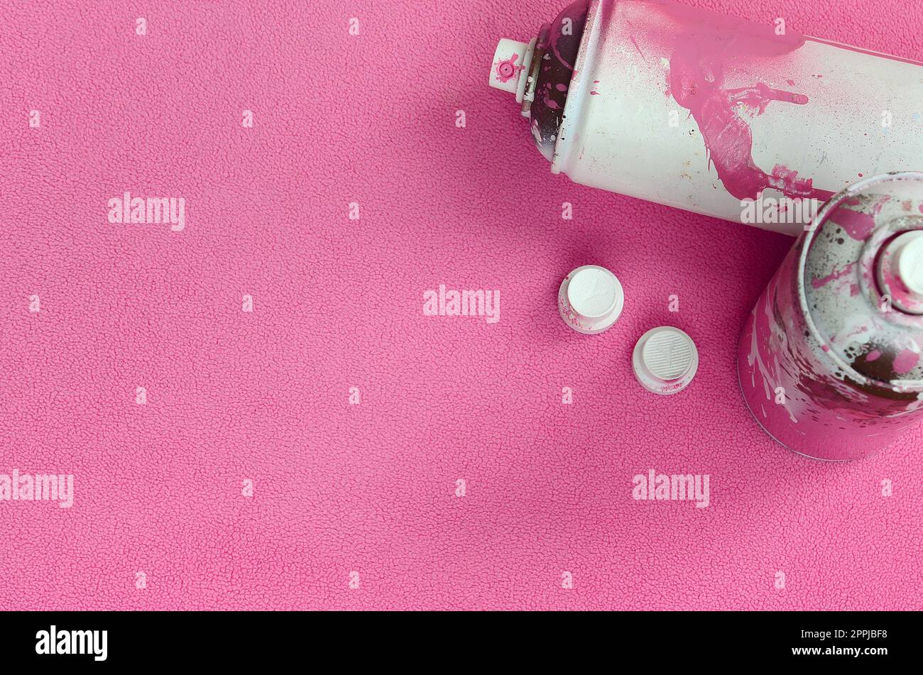 Einige gebrauchte rosafarbene Spraydosen und Düsen mit Lacktropfen liegen auf einer Decke aus weichem und pelzigem hellrosa Vlies. Klassische Damenfarbe. Graffiti-Hooliganismus-Konzept Stockfoto