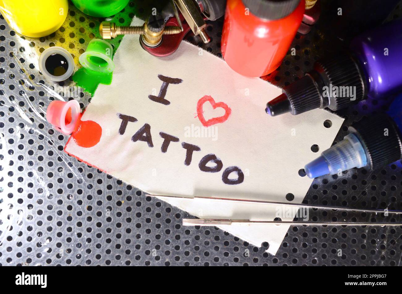 Ich liebe Tattoo. Der Text ist auf einem kleinen Blatt Papier unter verschiedenen Geräten zum Tätowieren geschrieben Stockfoto