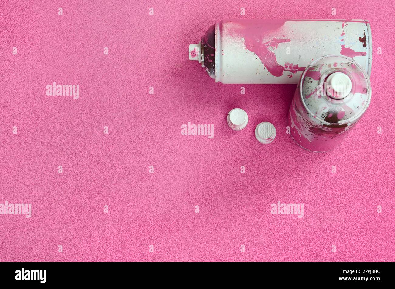 Einige gebrauchte rosafarbene Spraydosen und Düsen mit Lacktropfen liegen auf einer Decke aus weichem und pelzigem hellrosa Vlies. Klassische Damenfarbe. Graffiti-Hooliganismus-Konzept Stockfoto