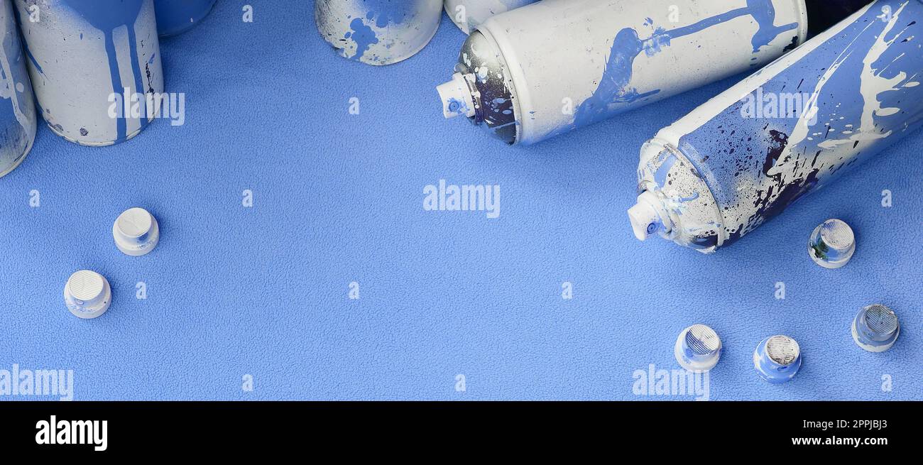 Einige gebrauchte blaue Spraydosen und Düsen mit Lacktropfen liegen auf einer Decke aus weichem, hellblauem Fleece. Klassische Damenfarbe. Graffiti-Hooliganismus-Konzept Stockfoto