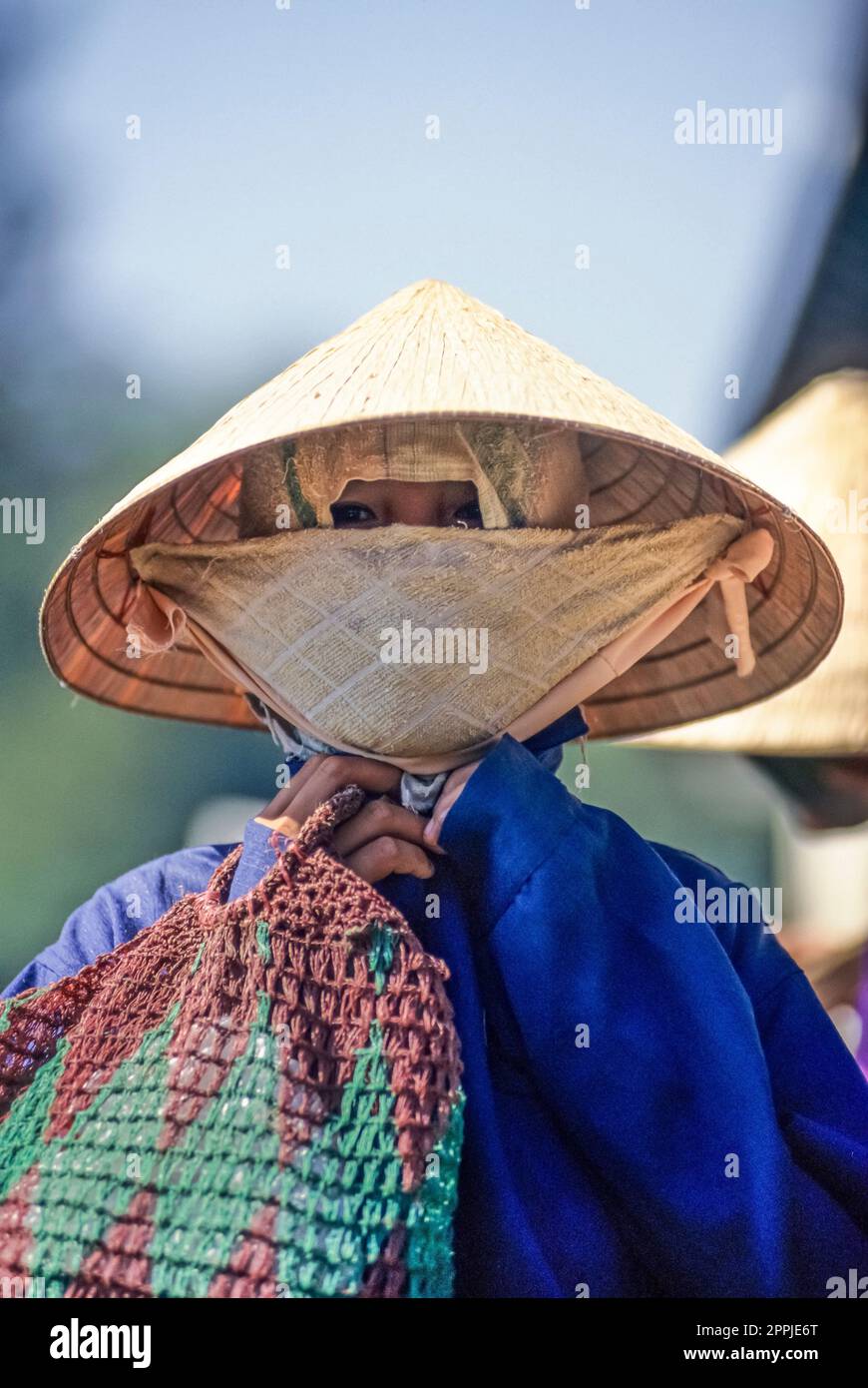 Gescannte Folie mit historischem Farbfoto einer nicht wiedererkennbaren Frau in Vietnam, die Reismütze und Staubmaske trägt Stockfoto