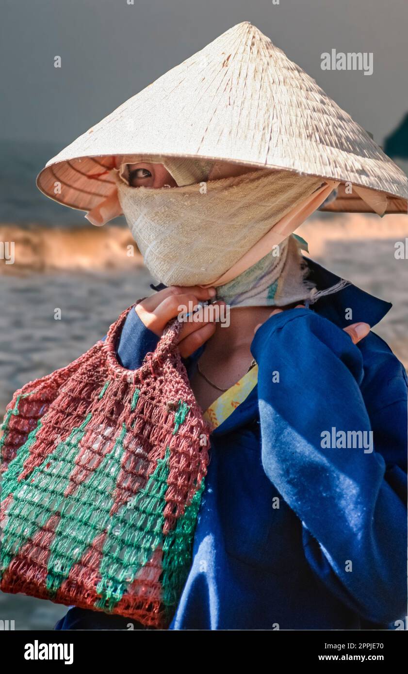 Gescannte Folie mit historischem Farbfoto einer nicht wiedererkennbaren Frau in Vietnam, die Reismütze und Staubmaske trägt Stockfoto