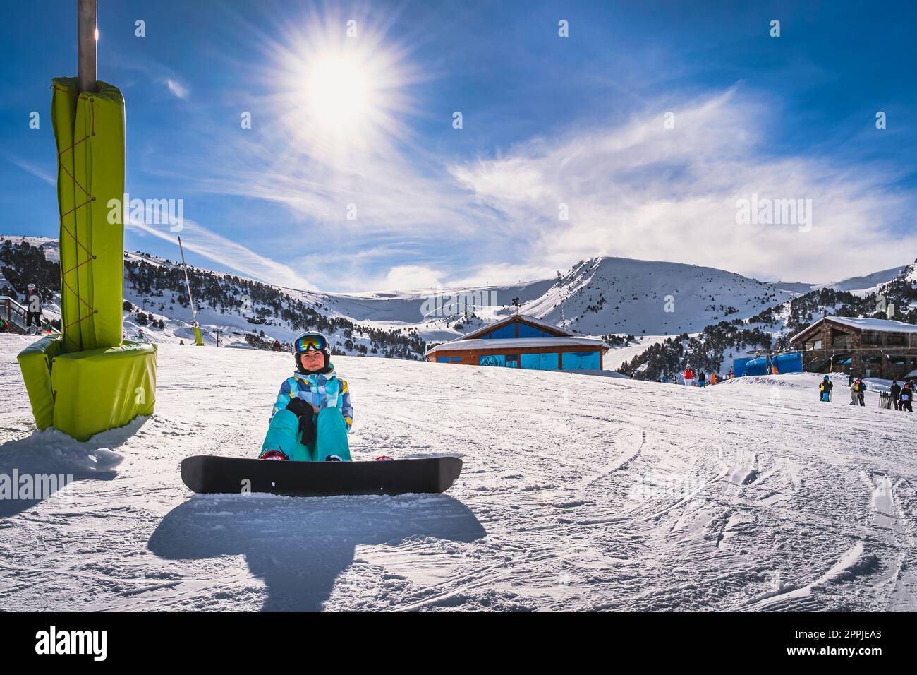 Porträt einer Snowboarderin, die auf Schnee sitzt und in die Kamera schaut, Andorra Stockfoto