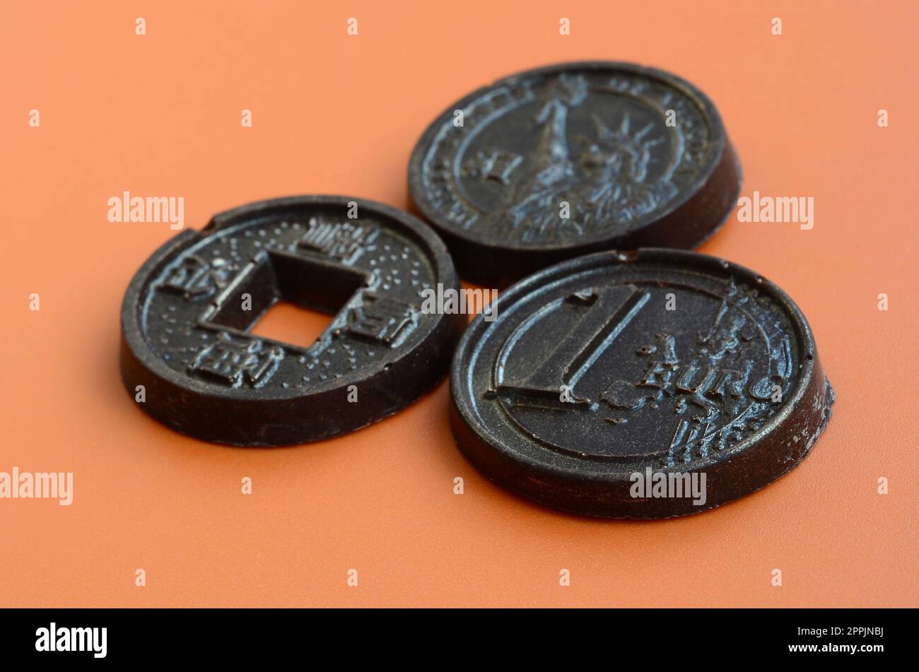 Drei Schokoladenerzeugnisse in Form von Euro-, USA- und Japan-Münzen liegen auf orangefarbenem Kunststoffhintergrund. Ein Modell von Bargeld-Münzen in essbarer Form Stockfoto
