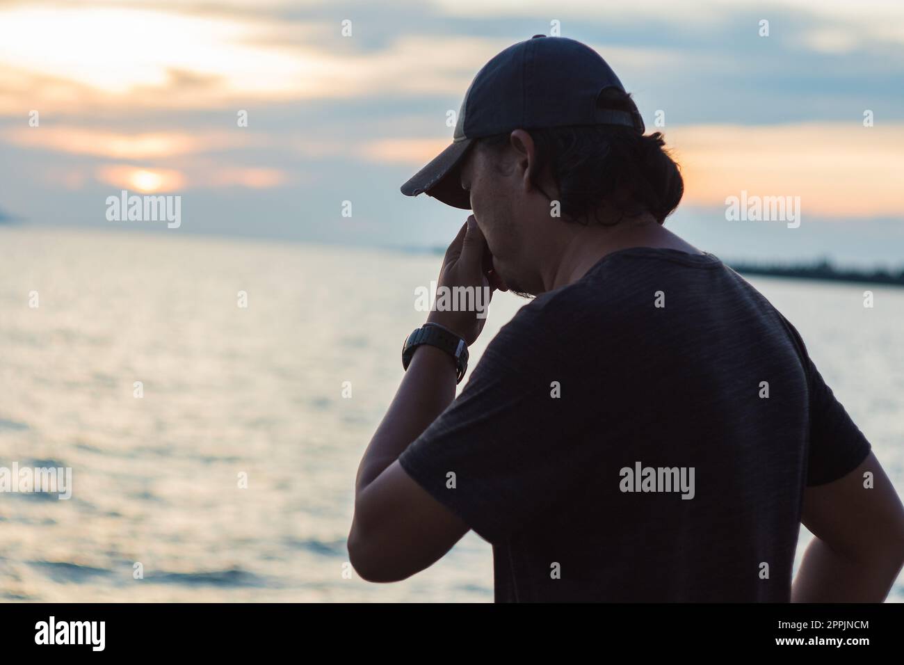 Silhouette eines Mannes, der mit dem Sonnenuntergang im wunderschönen Meer steht Stockfoto