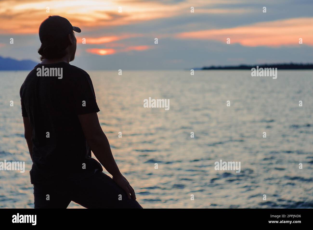 Silhouette eines Mannes, der mit dem Sonnenuntergang im wunderschönen Meer steht Stockfoto