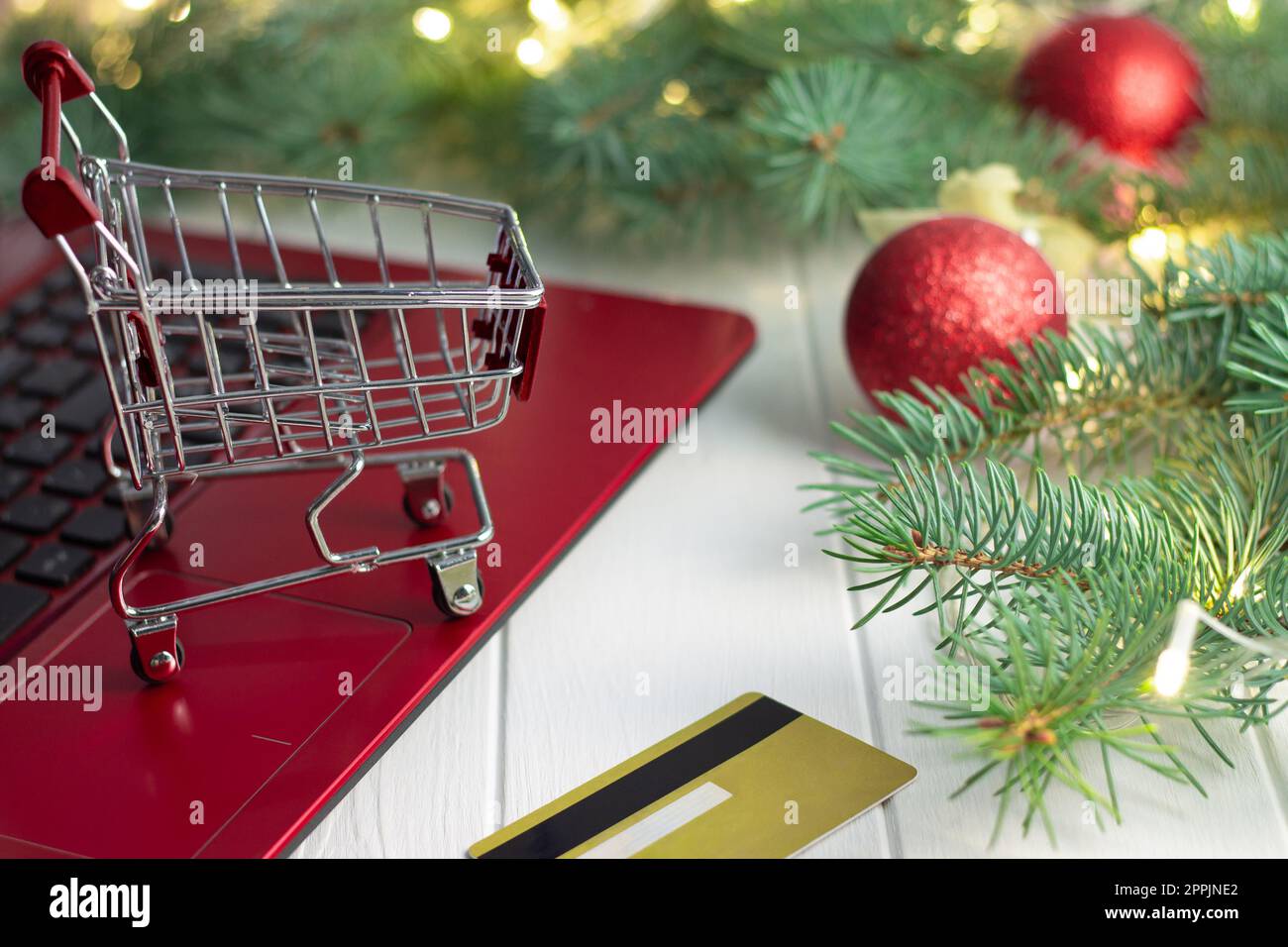 Einkaufswagen auf Laptop-Tastatur, Kreditkarte, Zweige von Weihnachtsbäumen mit Glühbirnen und Kugeln auf weißem Hintergrund Stockfoto