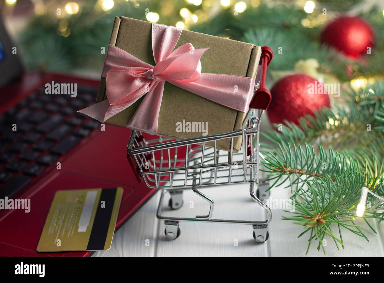 Einkaufswagen mit Geschenk, Tastatur mit Laptop, Kreditkarte, Zweigen eines Weihnachtsbaums, Bälle auf weißem Hintergrund Stockfoto
