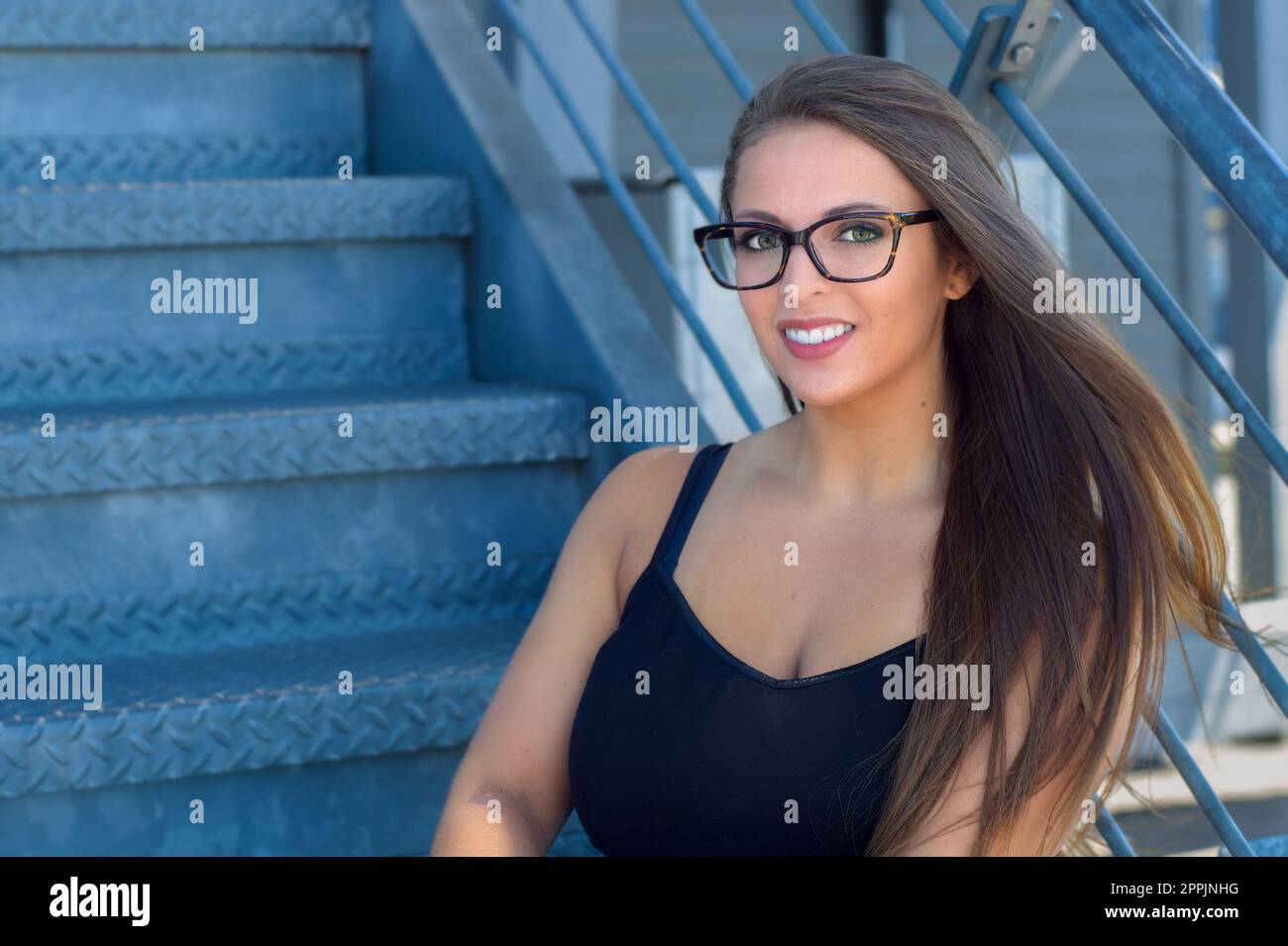Junge Frau, die auf einer Metalltreppe vor dem Lifestyle-Lächeln sitzt und Student 20s ist Stockfoto