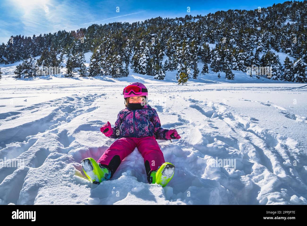 Lächelndes Mädchen, das auf frischem Schnee sitzt, mit Bergen und Wald im Hintergrund, Andorra Stockfoto