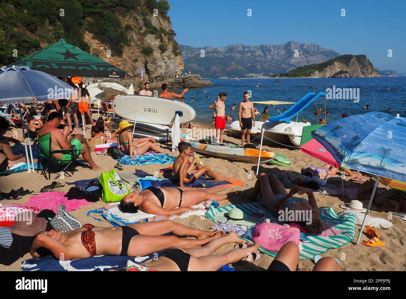 Budva, Montenegro, Mogren Beach. August 15 2022 Sand- und Kieselstrand in der Nähe hoher Klippen. Sonnenschirme, Cafes, Liegestühle. Die Leute entspannen sich, schwimmen, genießen Stockfoto