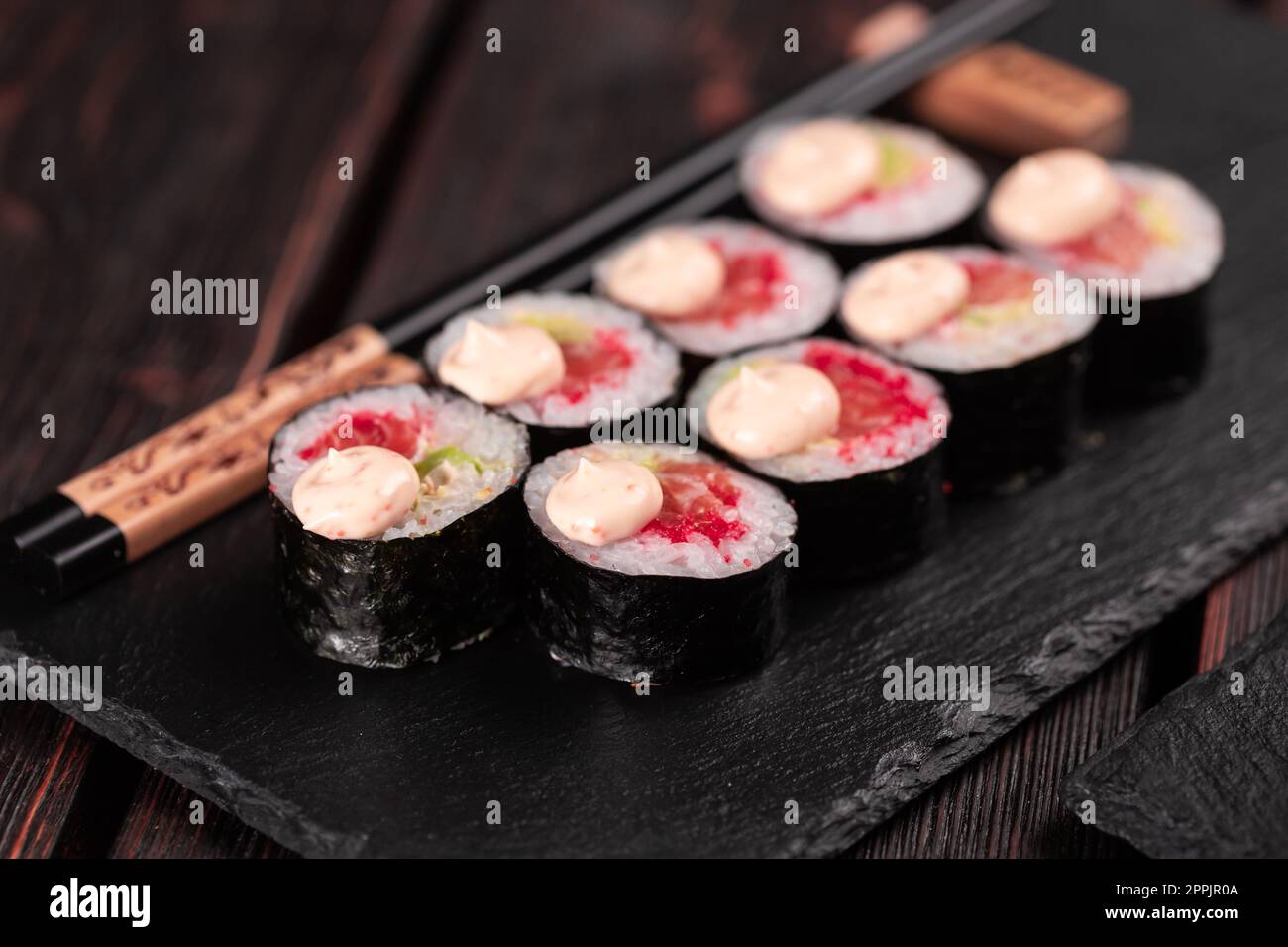 Maki Sushi-Brötchen mit Lachs-Avocado und Tobiko-Kaviar, serviert auf schwarzem Brett aus nächster Nähe - japanische Küche Stockfoto