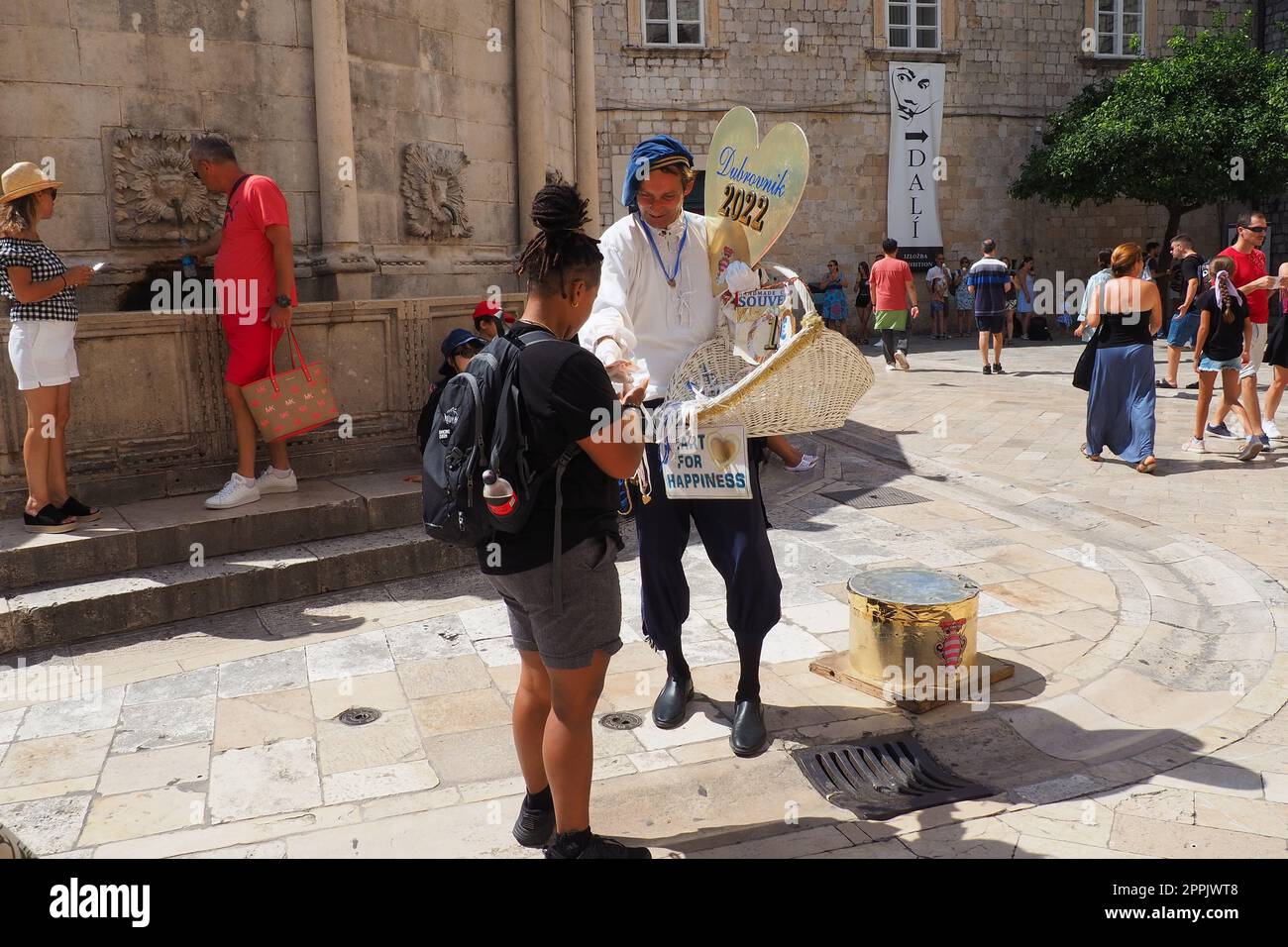 Auf den Straßen von Dubrovnik Kroatien gehen glückliche Urlauber zu Fuß und kaufen Souvenirs vom Verkäufer in dem nationalen kroatischen Festkostüm am 15. August 2022. Tourismusbranche. Sommertag. Verkauf von Waren Stockfoto