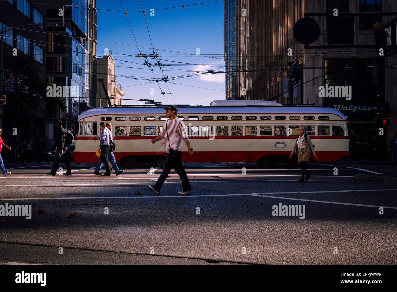 San Francisco, Kalifornien, USA, November 2013: Menschen, die die Straßen von San Francisco durchqueren, klassische Straßenbahn im Hintergrund, am blauen Himmel. Stockfoto