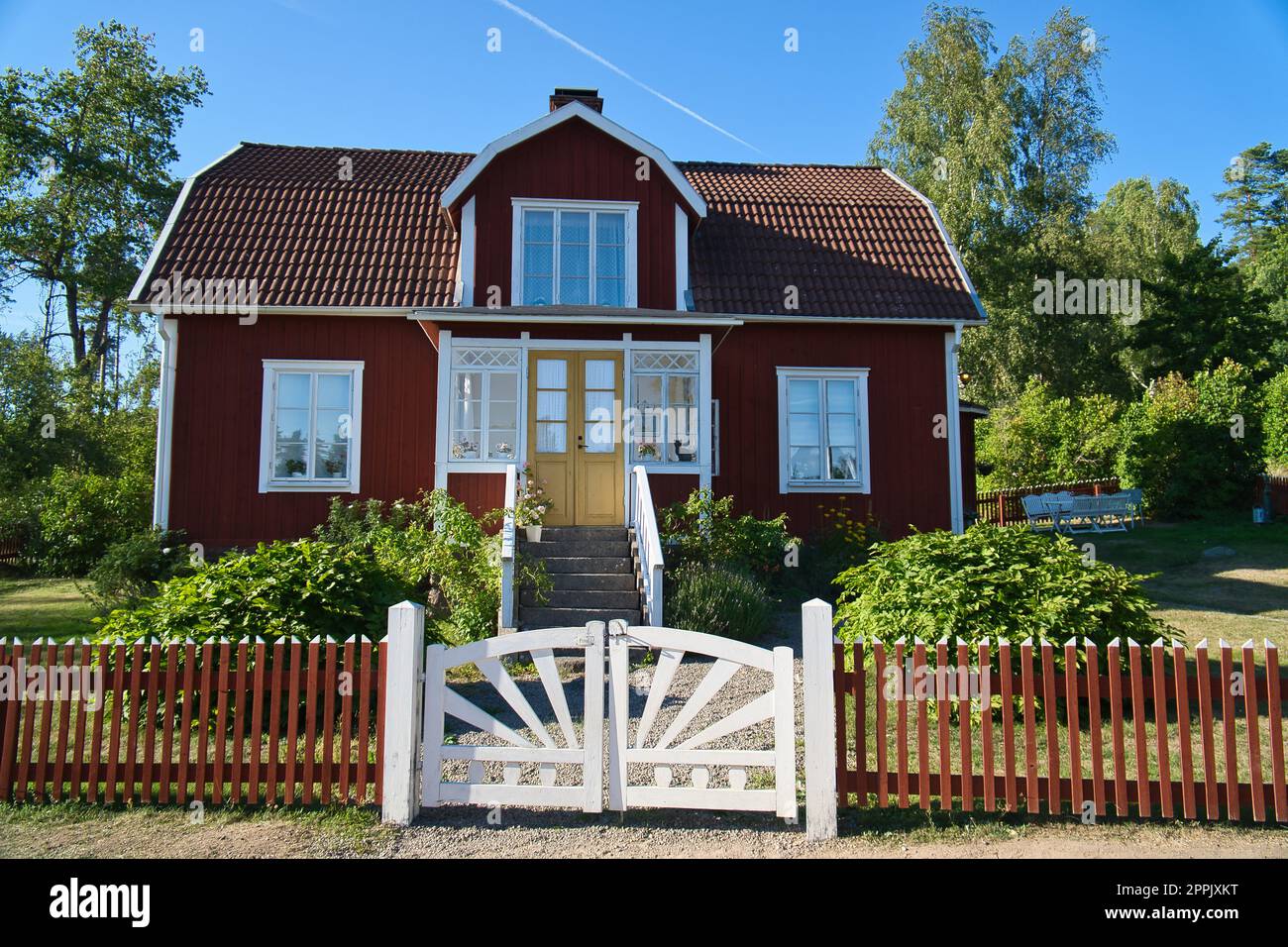 Traditionelles schwedisches rot-weißes Haus in Smalland, weißer Zaun, grüner Garten, blauer Himmel Stockfoto