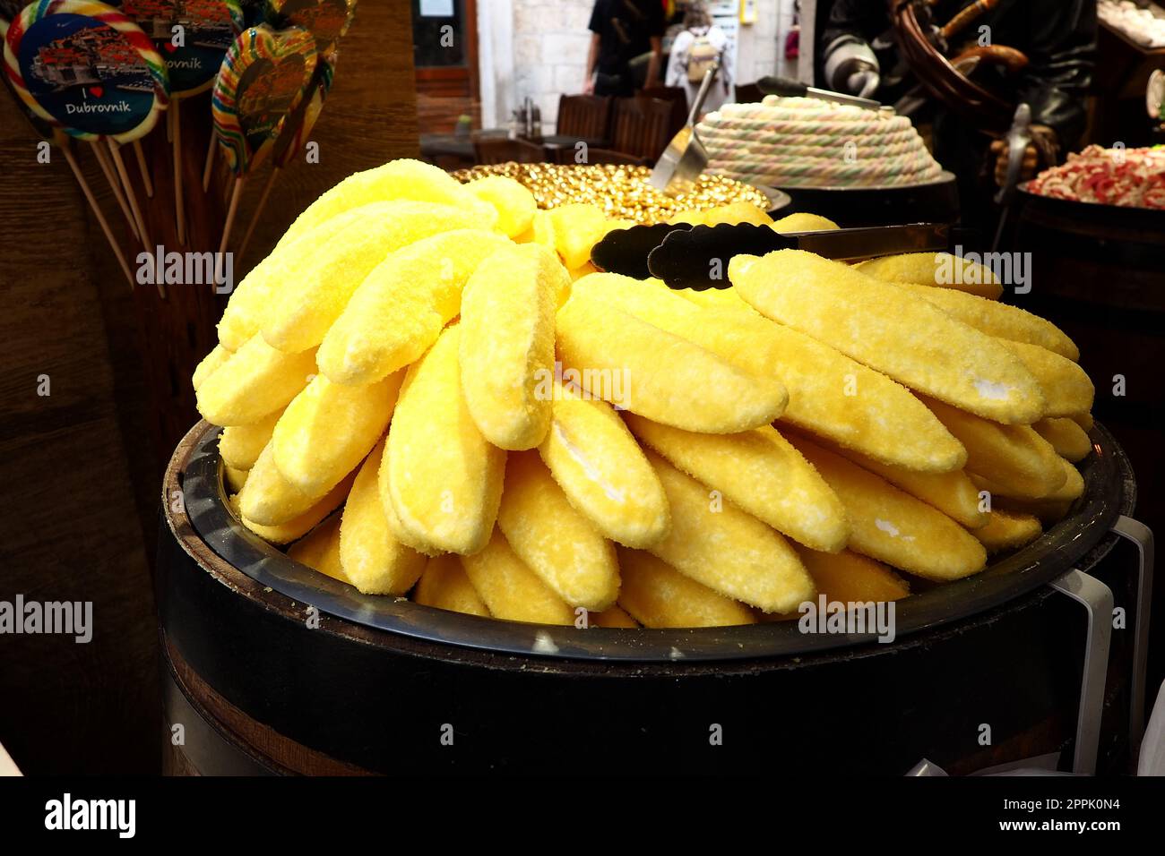 Eclairs in Form von gelben Bananen auf einem Gericht. Ein Schaukasten des Süßigkeitenladens Dubrovnik Croatia. Leckere süße Kuchen werden Touristen zum Verkauf angeboten. Ungewöhnliche Form des Backens mit pulvergelbem Zucker. Stockfoto