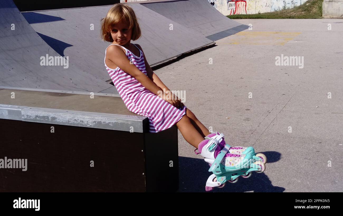 Sremska Mitrovica, Serbien, 12. September 2020. Das Mädchen fährt Rollerblading auf dem Asphalt. Ein 7-jähriges Kind in einem gestreiften weißen und pinkfarbenen Kleid fährt auf Rollschuhen auf dem Spielplatz. Stockfoto