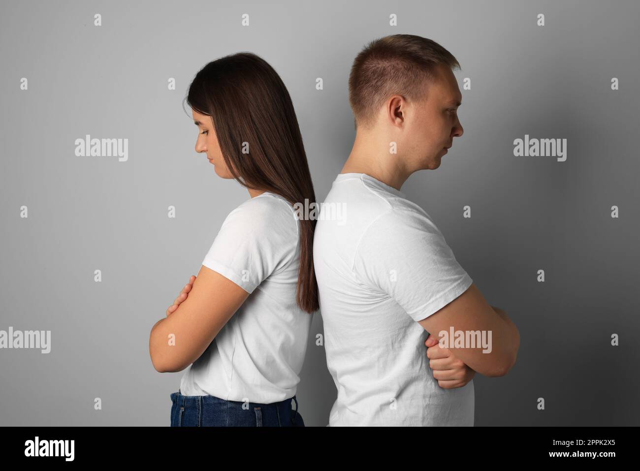 Unglückliches junges Paar, das sich vor hellem Hintergrund den Rücken zudreht Stockfoto