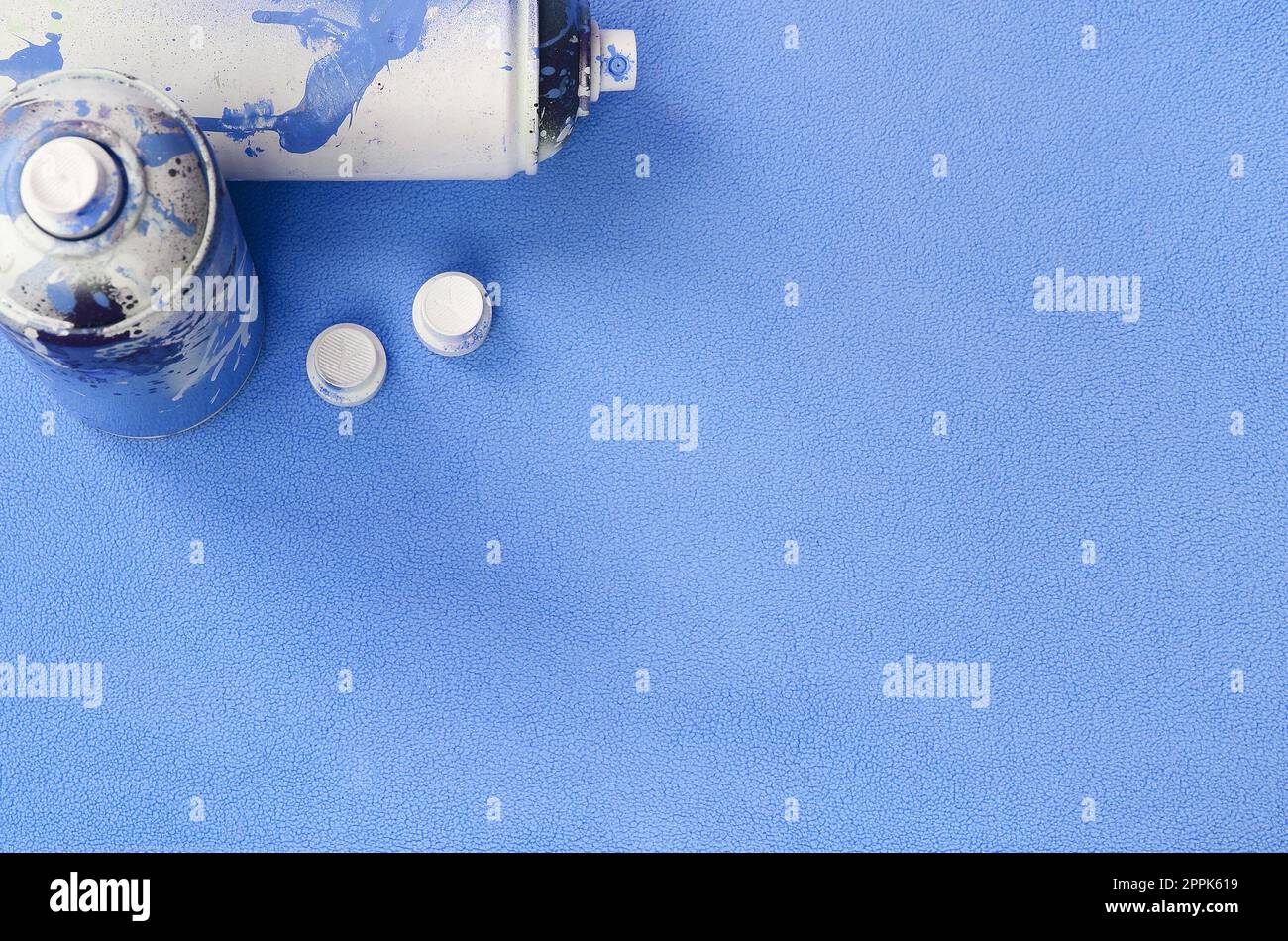 Einige gebrauchte blaue Spraydosen und Düsen mit Lacktropfen liegen auf einer Decke aus weichem, hellblauem Fleece. Klassische Damenfarbe. Graffiti-Hooliganismus-Konzept Stockfoto