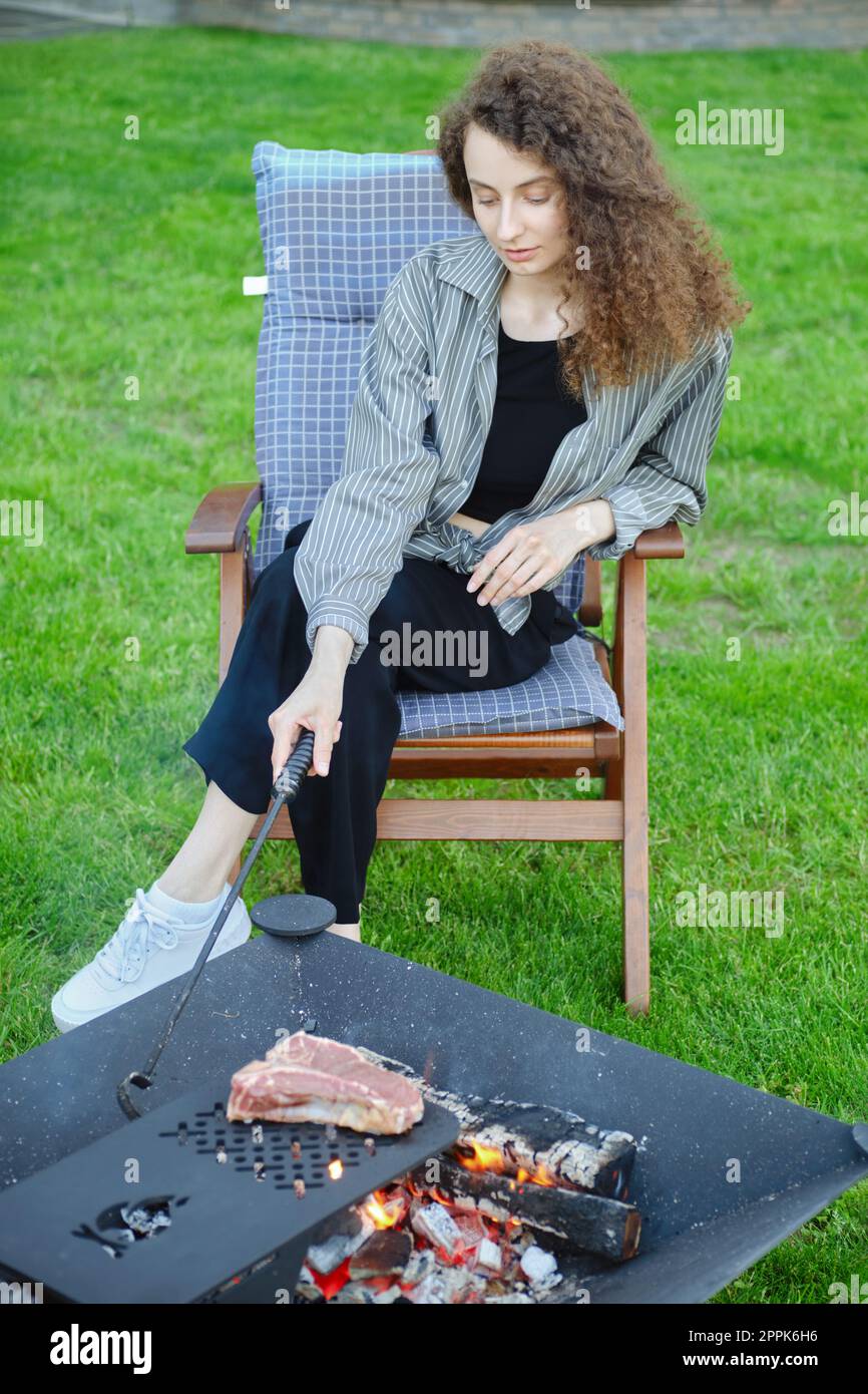 Eine Frau rührt die Kohlen, während sie ein Steak auf dem Grill kocht Stockfoto
