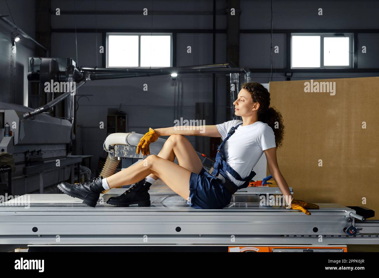 Die Frau sitzt auf einem Geländer einer Kreissäge einer holzbearbeitenden Maschine Stockfoto