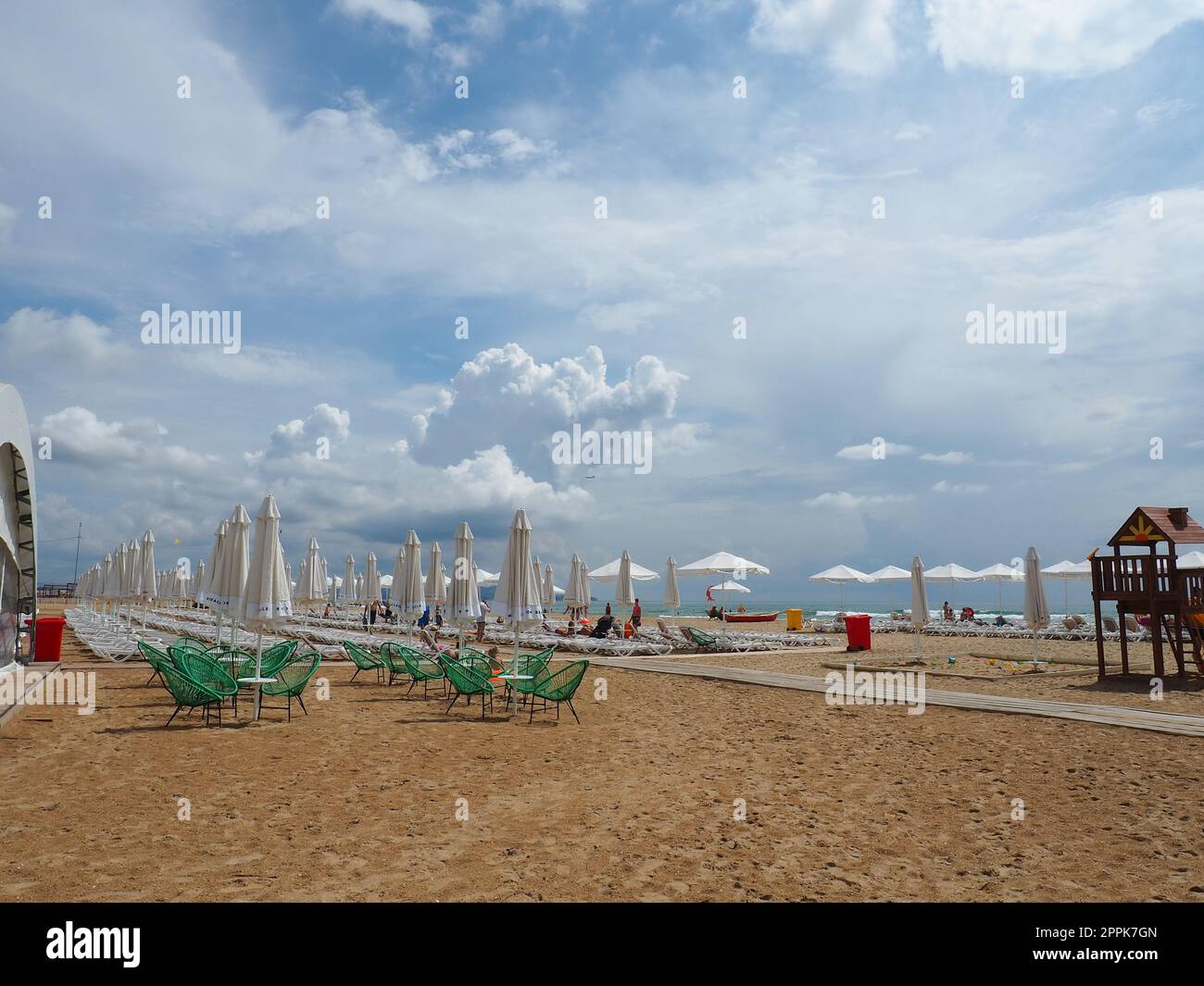 Anapa, Russland, 15. August 2021 Sonnenliegen und Sonnenschirme am Sandstrand nach dem Regen. Strandsaison. Strandcafe mit Korbstühlen. Touristen, die Leute laufen lassen. Eine Sturmwarnung. Kumuluswolken Stockfoto