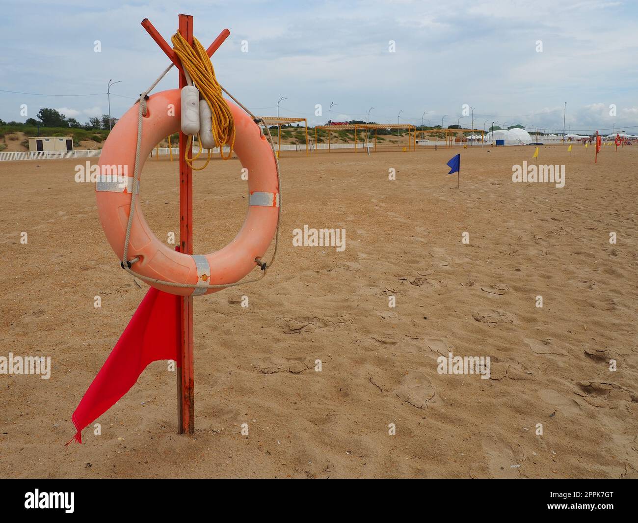 Anapa, Russland, 10. August 2021 Lifebuoy mit einer roten Flagge an einem Sandstrand. Orangefarbenes Rettungsboot an einer Stange, um Menschen zu retten, die im Meer ertrinken. Rettungspunkt am Ufer. Stürmisches Wetter am Schwarzen Meer Stockfoto