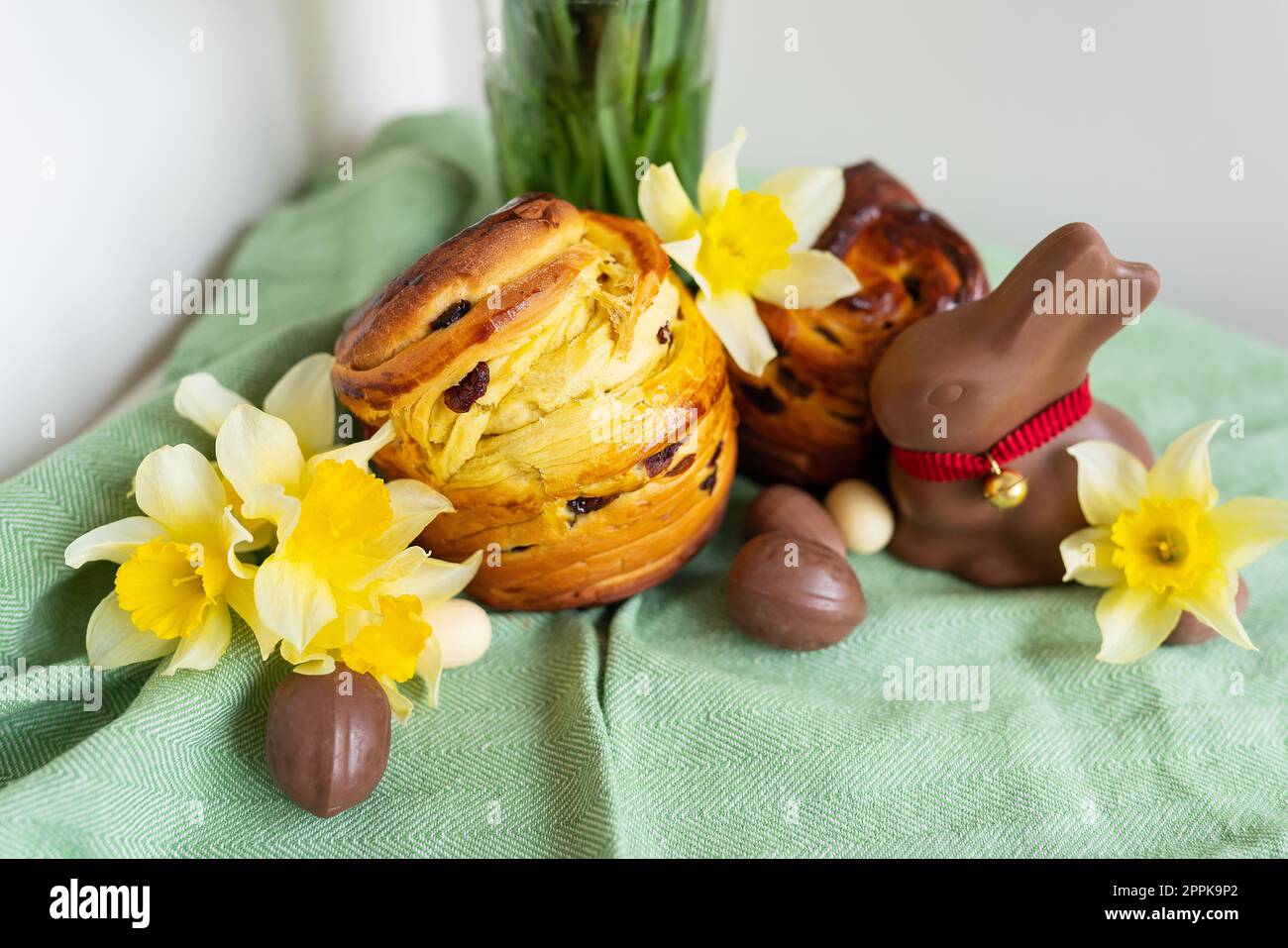 Hausgemachtes traditionelles Ostergebäck liegt auf einer grünen Serviette zusammen mit Narzissen, Kaninchen und Schokoladeneiern. Osterbacken und Dekoration. Stockfoto