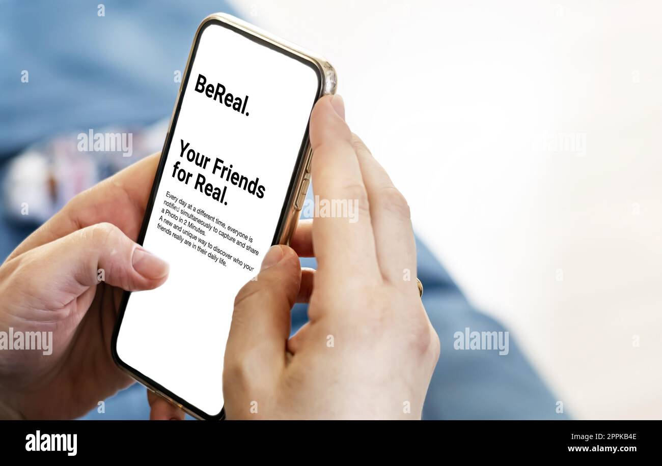 Weibliche Hände halten ein Telefon mit dem Bereal. Mobile App auf dem Bildschirm Stockfoto