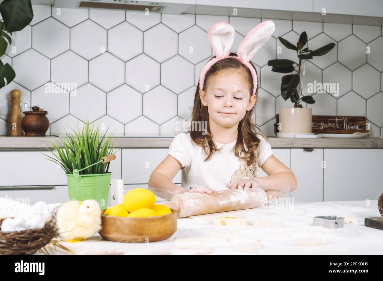 Portrait eines kleinen, lächelnden, studiotisch gelaunten Mädchens, kochen, Teig zubereiten, Nadeln mit Mehl Rollen. Ich mache osterbackkekse Stockfoto