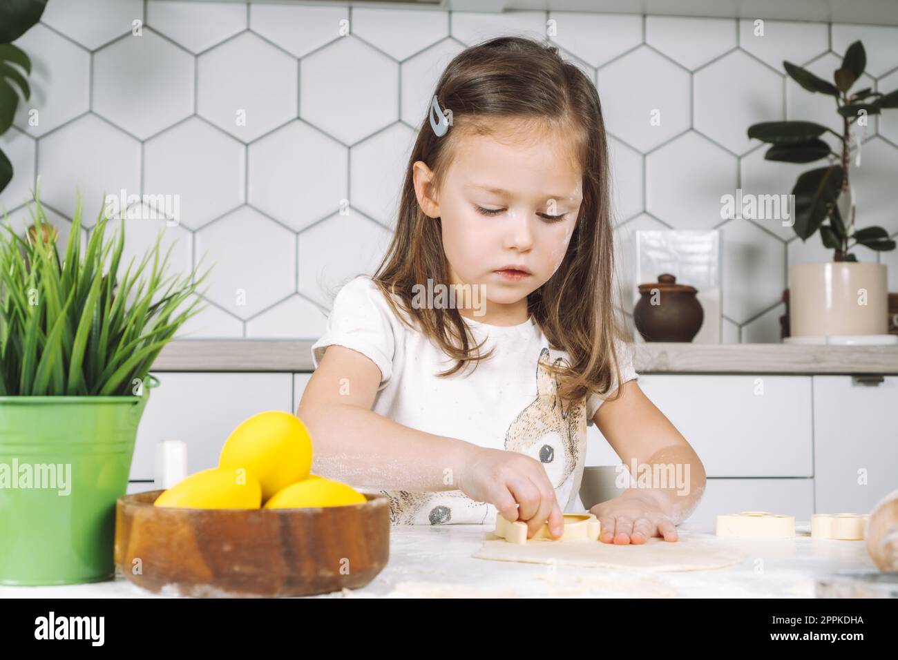 Porträt eines freudigen, konzentrierten kleinen Mädchens, geformter Teigkeks, Backbecher. Vorbereitung auf Osterfeiertage Stockfoto