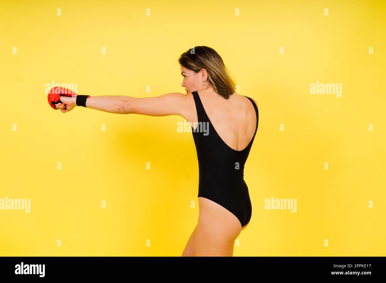 Starke Sportlerin in Boxhandschuhen bereitete High-Kick vor. Isoliert auf weißem, rotem, gelbem Hintergrund Stockfoto
