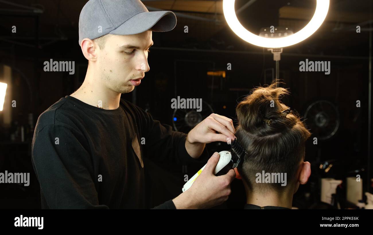 Friseur und Haarschneider für Herren mit Haarschneider in einem Friseur oder Friseursalon. Friseurservice in einem modernen Friseursalon mit dunklem Licht und Blick nach hinten Stockfoto