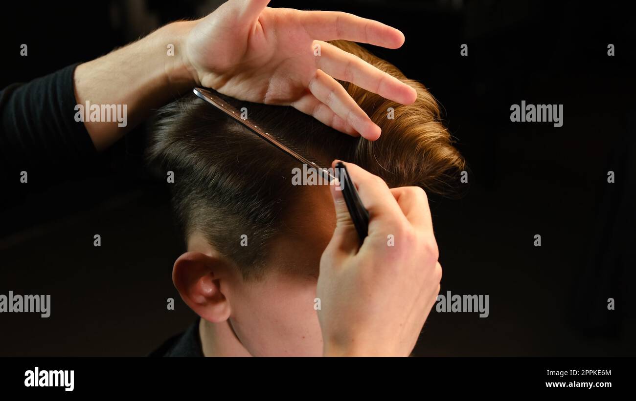 Nahaufnahme des Friseurs mit Haarclip und Kamm zum Fixieren der Haare zum Schneiden und Stylen Frisör mit Pinne Friseursalon. Service in einem modernen Friseursalon mit dunklem Licht und Blick nach hinten Stockfoto