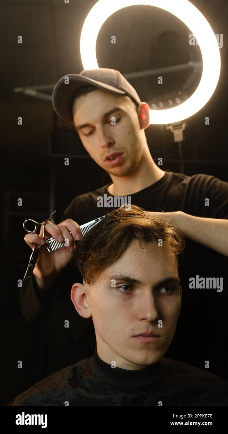 Friseurmeister Friseur frisiert und stylen mit Schere und Kamm. Concept Barbershop. Vorderansicht bei dunkler Tastenbeleuchtung mit warmem Licht Stockfoto