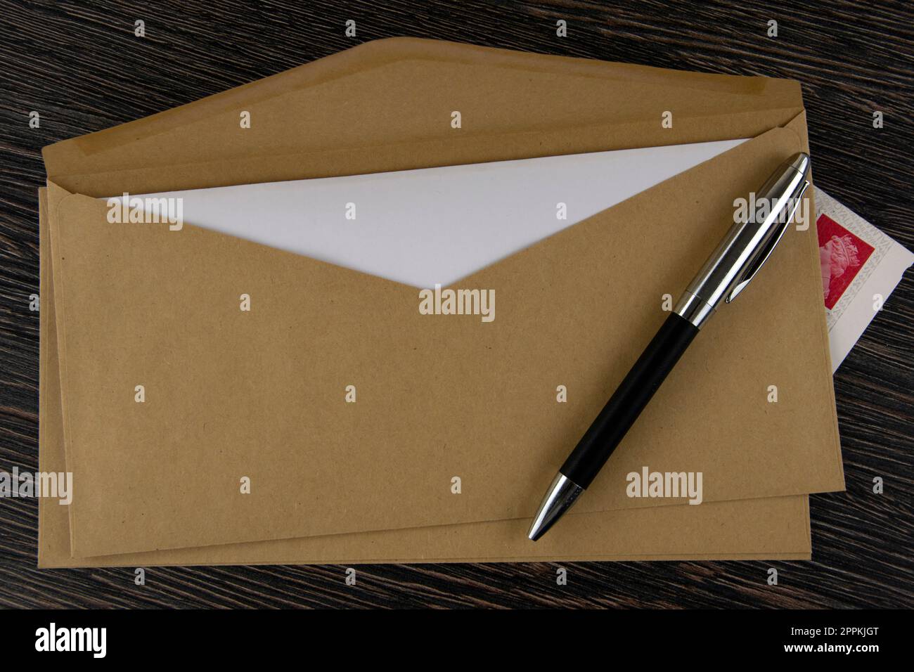 Brauner Umschlag, Stift und Briefmarken auf Holztisch Stockfoto