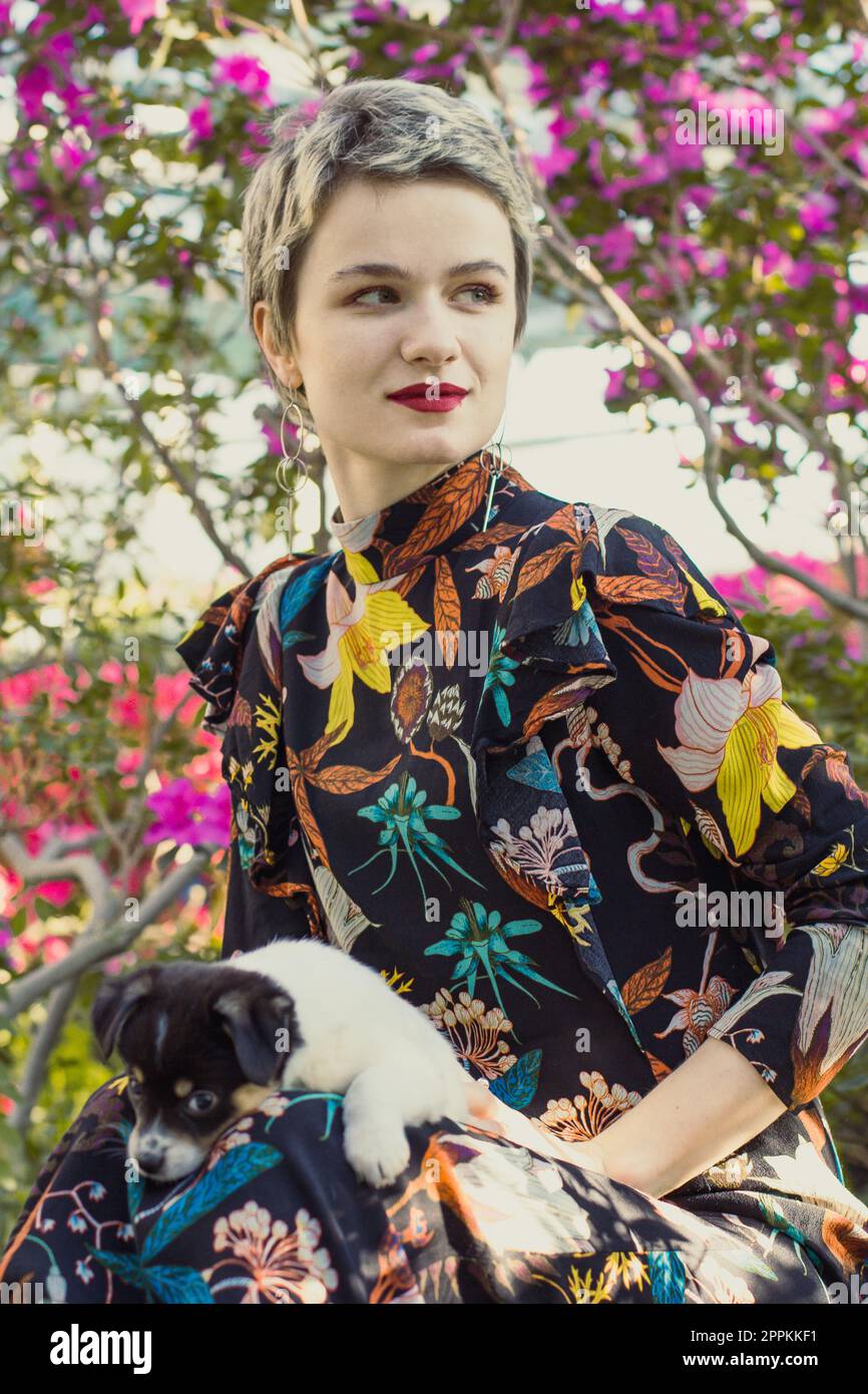 Nahaufnahme einer eleganten Frau mit kleinem Hündchen im blühenden Gartenporträt Stockfoto