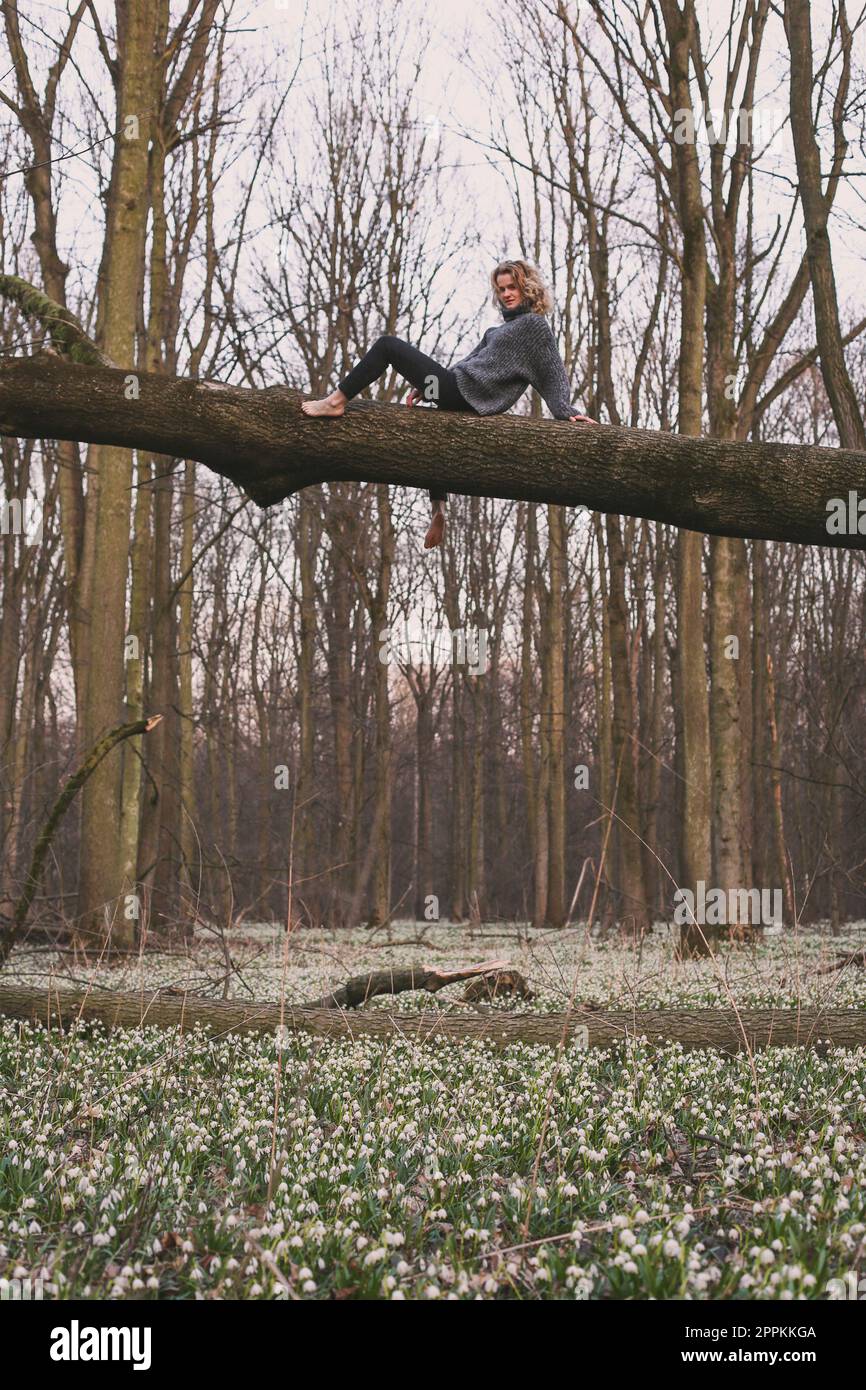 Blonder Barfußtourist, der auf einem Baumstamm sitzt, fotografiert Stockfoto