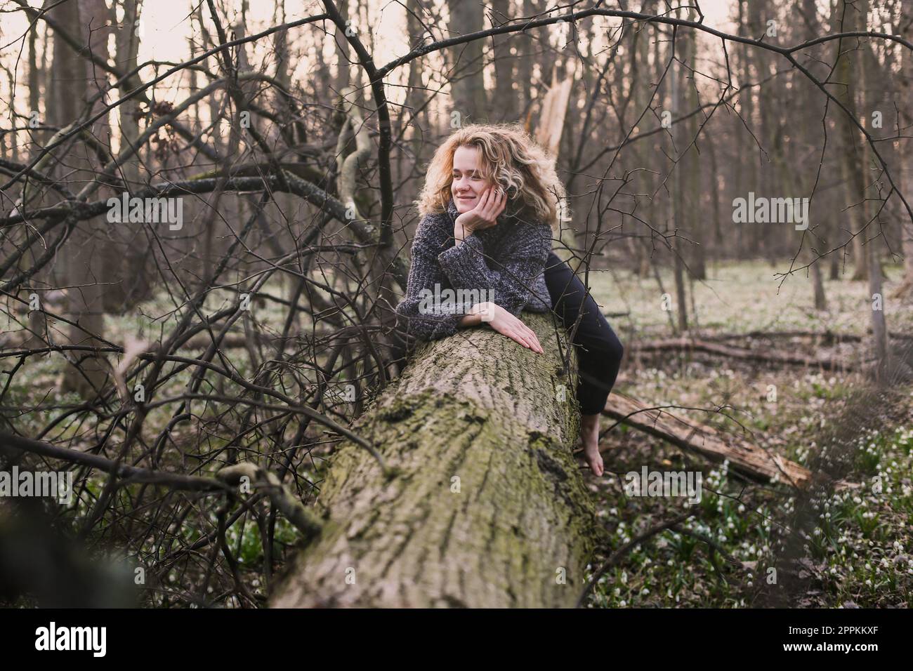 Eine lockige Frau, die sich auf dem Baumstamm ausruht, fotografiert Stockfoto