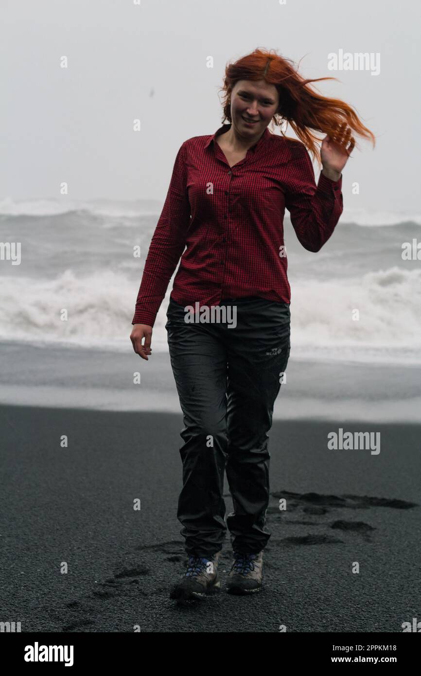 Frau mit unordentlichem Haar auf schwarzem Strand, malerische Fotografie Stockfoto