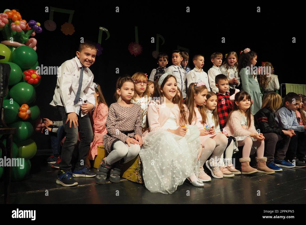 Sremska Mitrovica, Serbien, 8. März 2022 Kinderchorvorstellung auf der Bühne. Kinder singen. Musikalische Kindergruppe in eleganten Kostümen spielt Weihnachtslieder für Mütter. Dunkle Szene. Stockfoto