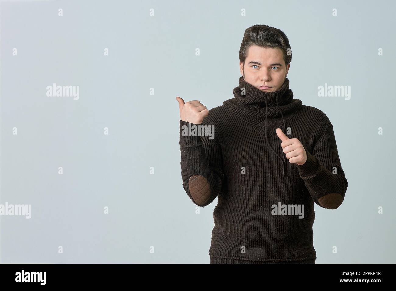 Ein Mann in einem braunen Pullover und einer leuchtenden Farbe zeigt auf etwas und perfekt, zeigt einen leeren Bereich mit seinem Daumen, zeigt alles auf einem hellen Hintergrund, Kopierbereich Stockfoto