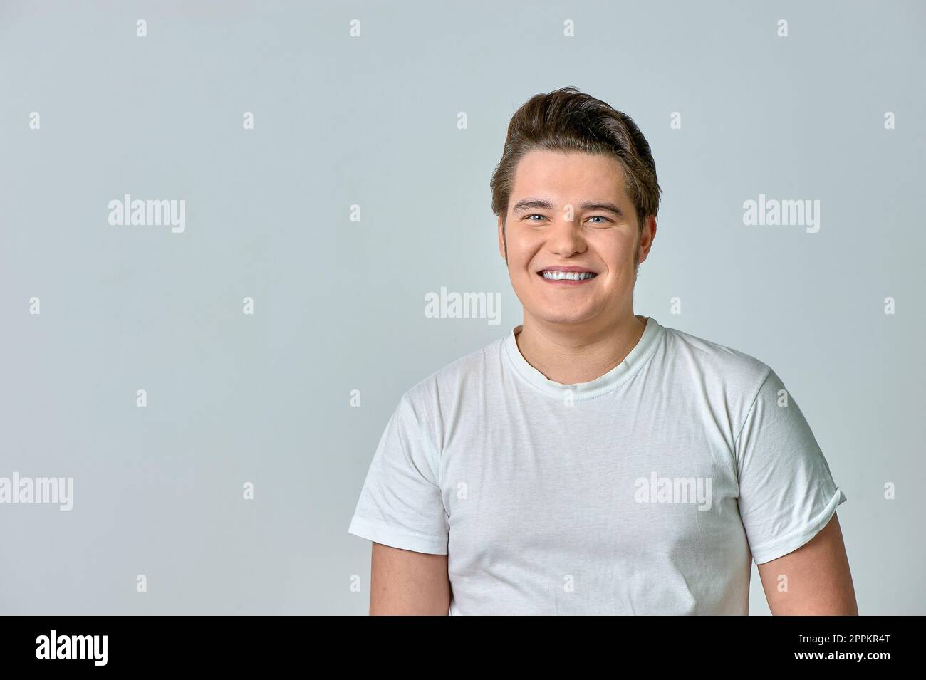 Ein Mann in einem weißen T-Shirt auf grauem Hintergrund lächelt Stockfoto