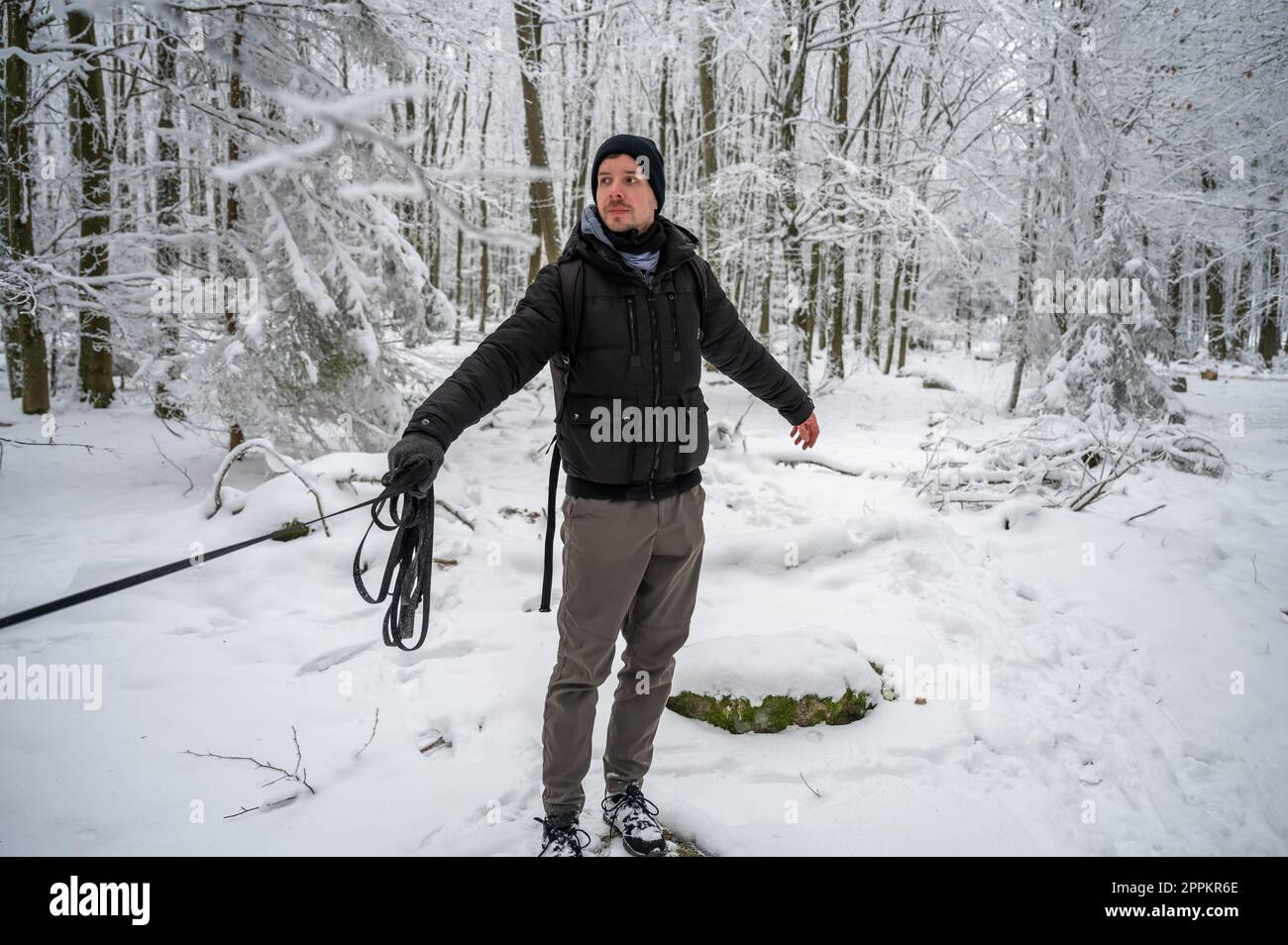 Ein Mann mit Bart und Hundeleine steht im Winter im Wald mit viel Schnee, ein Hund läuft davon, der Meister sieht seinen Hund an Stockfoto