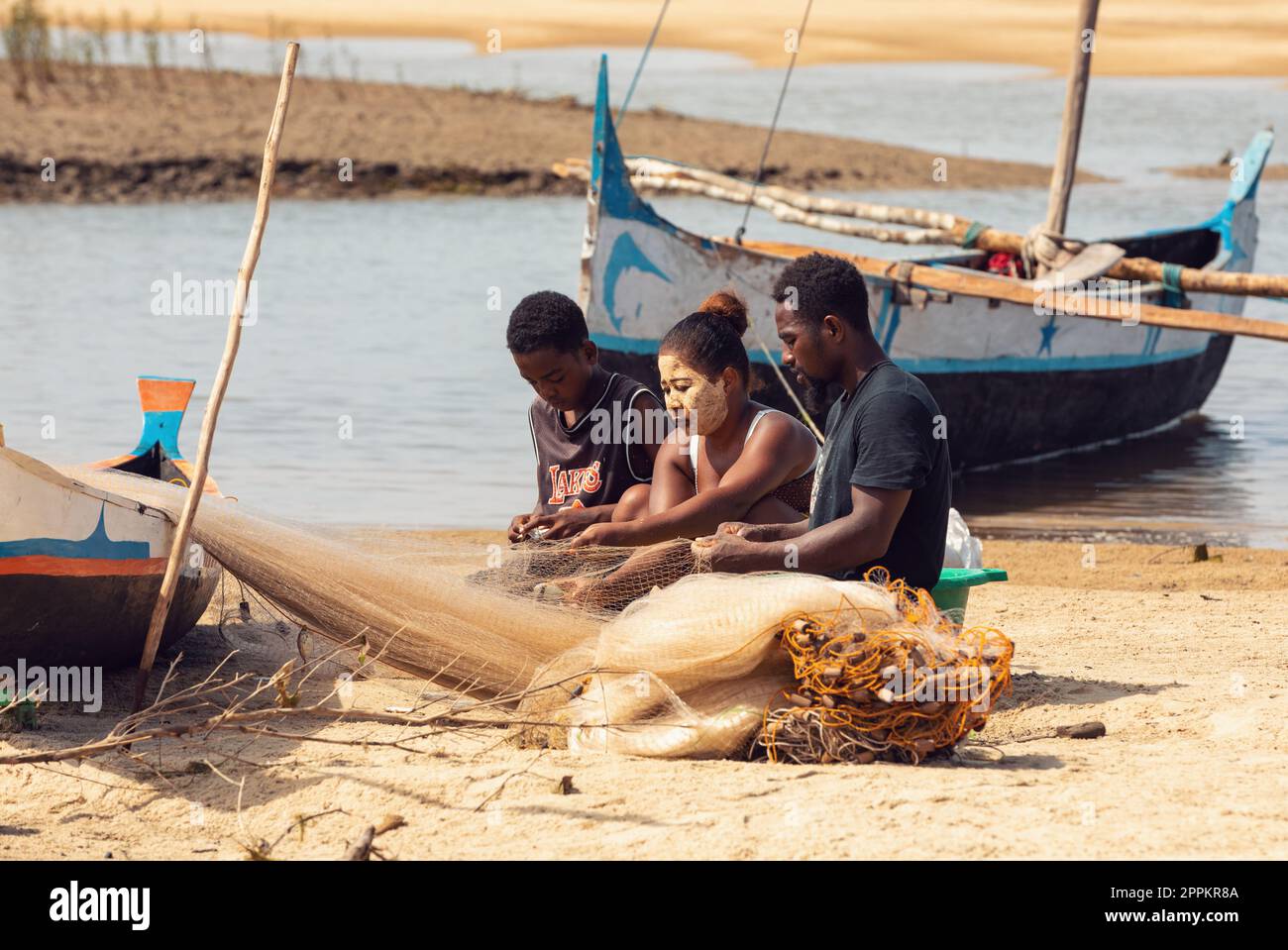 Fischer und Frauen reparieren Fischernetze an den Flussmündungen. Die Frau hat ein traditionell madagassisches Gesicht Stockfoto