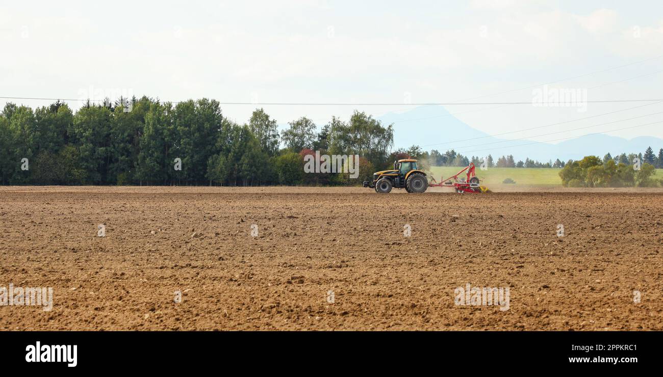 Traktor Aussaat im leeren Feld auf Landschaft mit Bergen im Hintergrund. Stockfoto