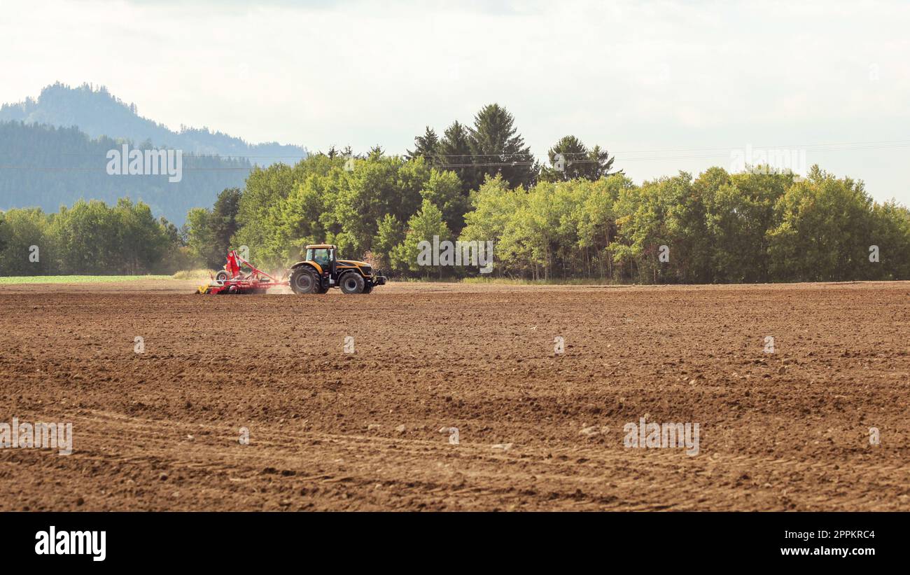 Traktor Aussaat im leeren Feld auf Landschaft, kleine Bäume im Hintergrund. Stockfoto