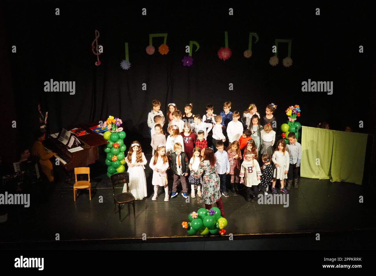 Sremska Mitrovica, Serbien, 8. März 2022 Kinderchorvorstellung auf der Bühne. Kinder singen. Musikalische Kindergruppe in eleganten Kostümen spielt Weihnachtslieder für Mütter. Dunkle Szene. Stockfoto